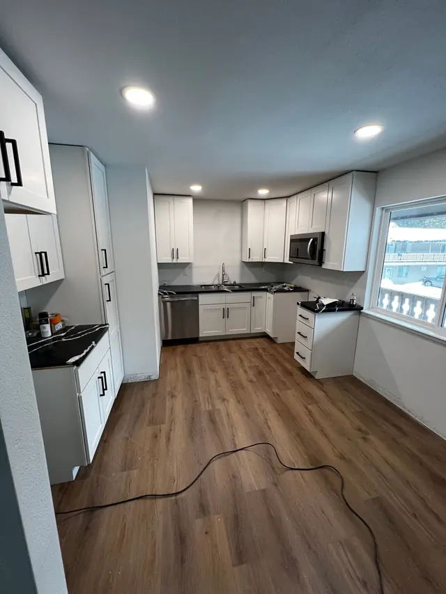 White shaker kitchen with black quartz counters and dark wood flooring