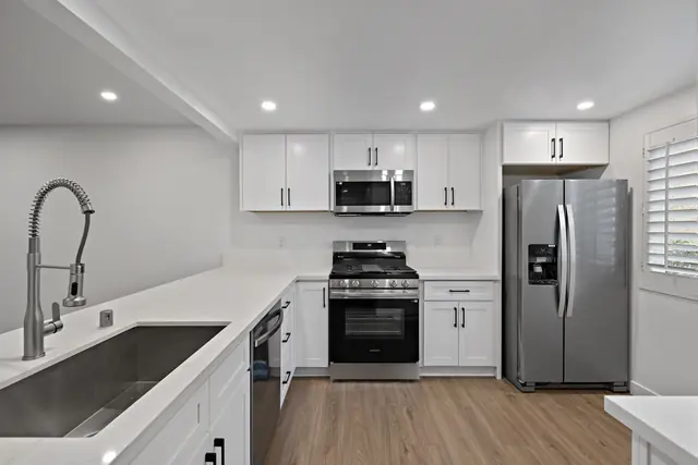 White shaker kitchen with quartz counters, a stainless range and refrigerator, and plantation shutters